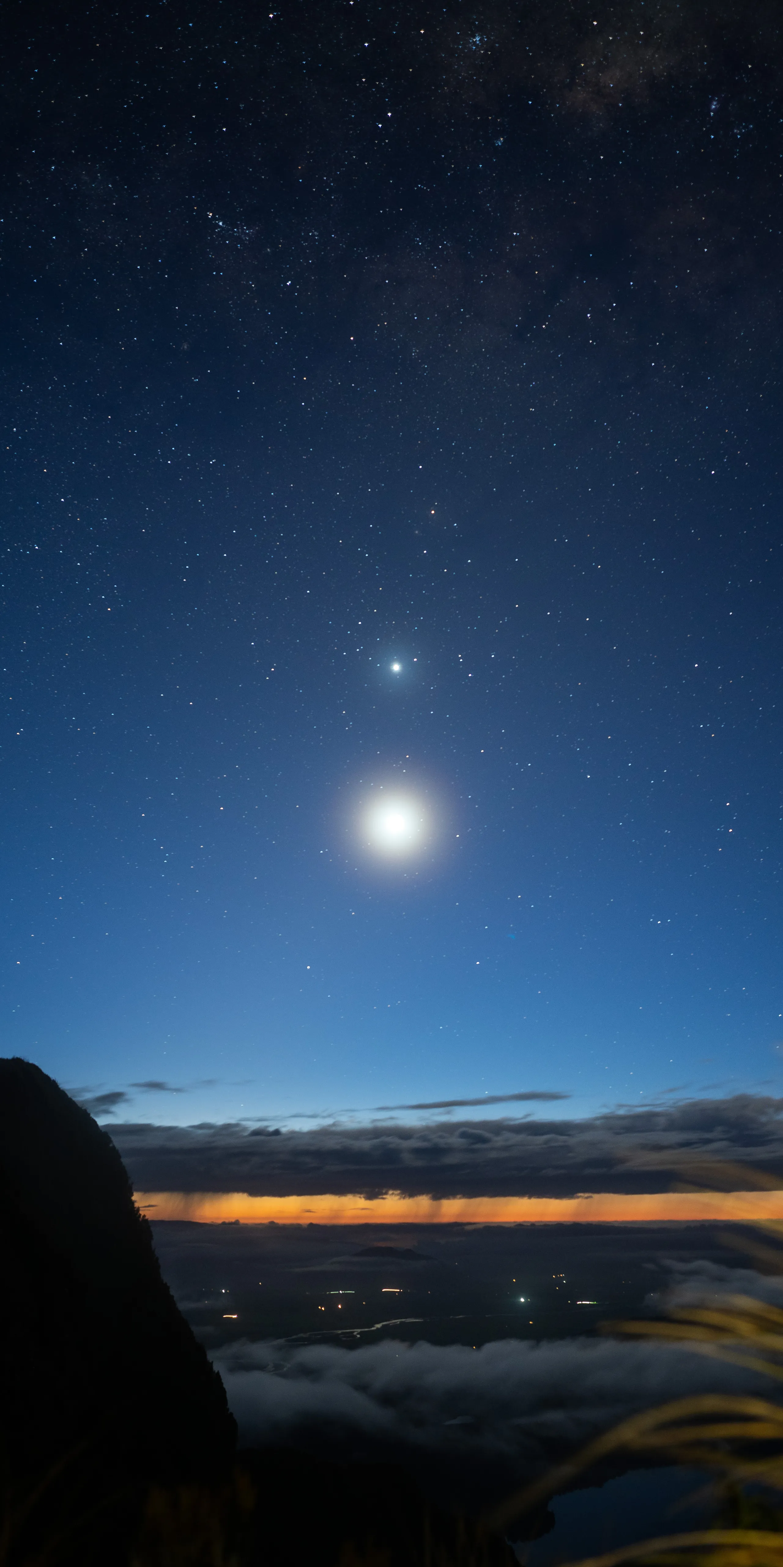 Moon and a planet after dusk. The lingering sunlight illuminates the rain below the distant clouds.